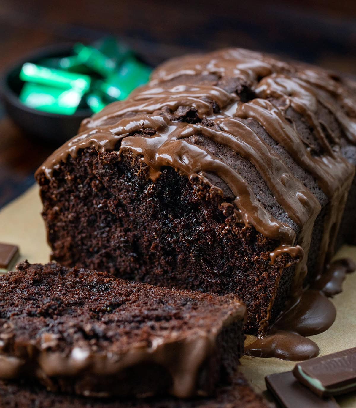 This Peppermint Brownie Bread is a rich and fudgy quick bread that is packed with chocolatey goodness with a refreshing hint of mint. It’s based on my popular brownie bread! Loaf of Peppermint Brownie Bread with some pieces cut and laying flat but close up with Ande's mints in the background.
