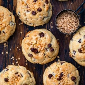 Thick and Chewy Chocolate Toffee Cookies on a wooden table with toffee bits from overhead.