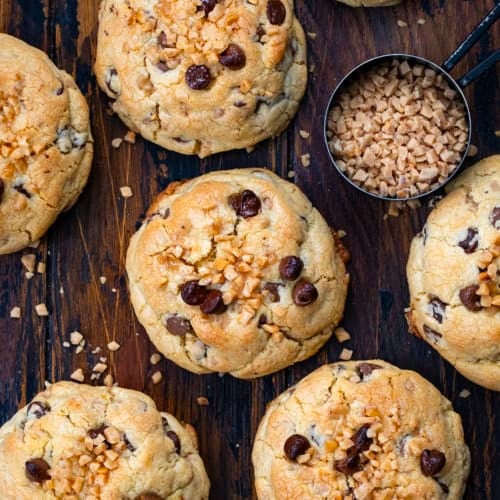 Thick and Chewy Chocolate Toffee Cookies on a wooden table with toffee bits from overhead.