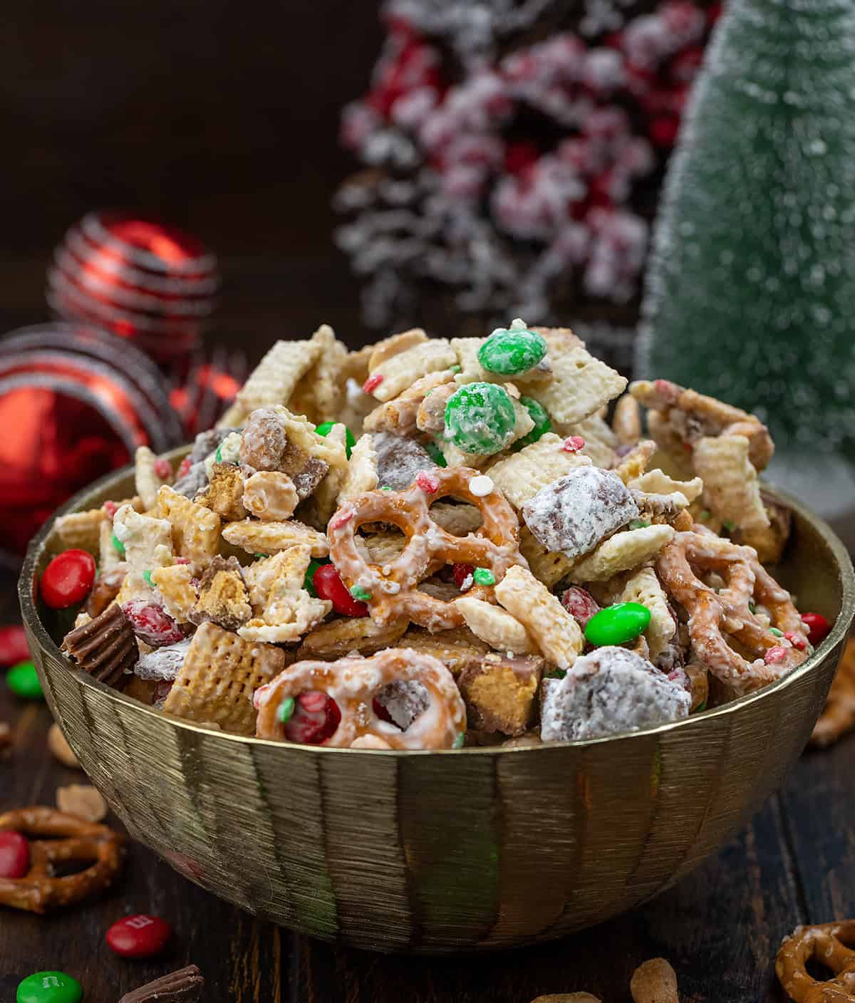 This Ultimate Christmas Snack Mix is what happens when all of my favorite holiday treats collide into one bowl. It’s sweet, salty, crunchy, and truly over-the-top... combining classic peanut butter puppy chow, glossy white chocolate-coated Chex, salty pretzels, peanuts, and festive holiday candies! Gold Bowl filled with Ultimate Christmas Snack Mix on a wooden table with Christmas decorations.