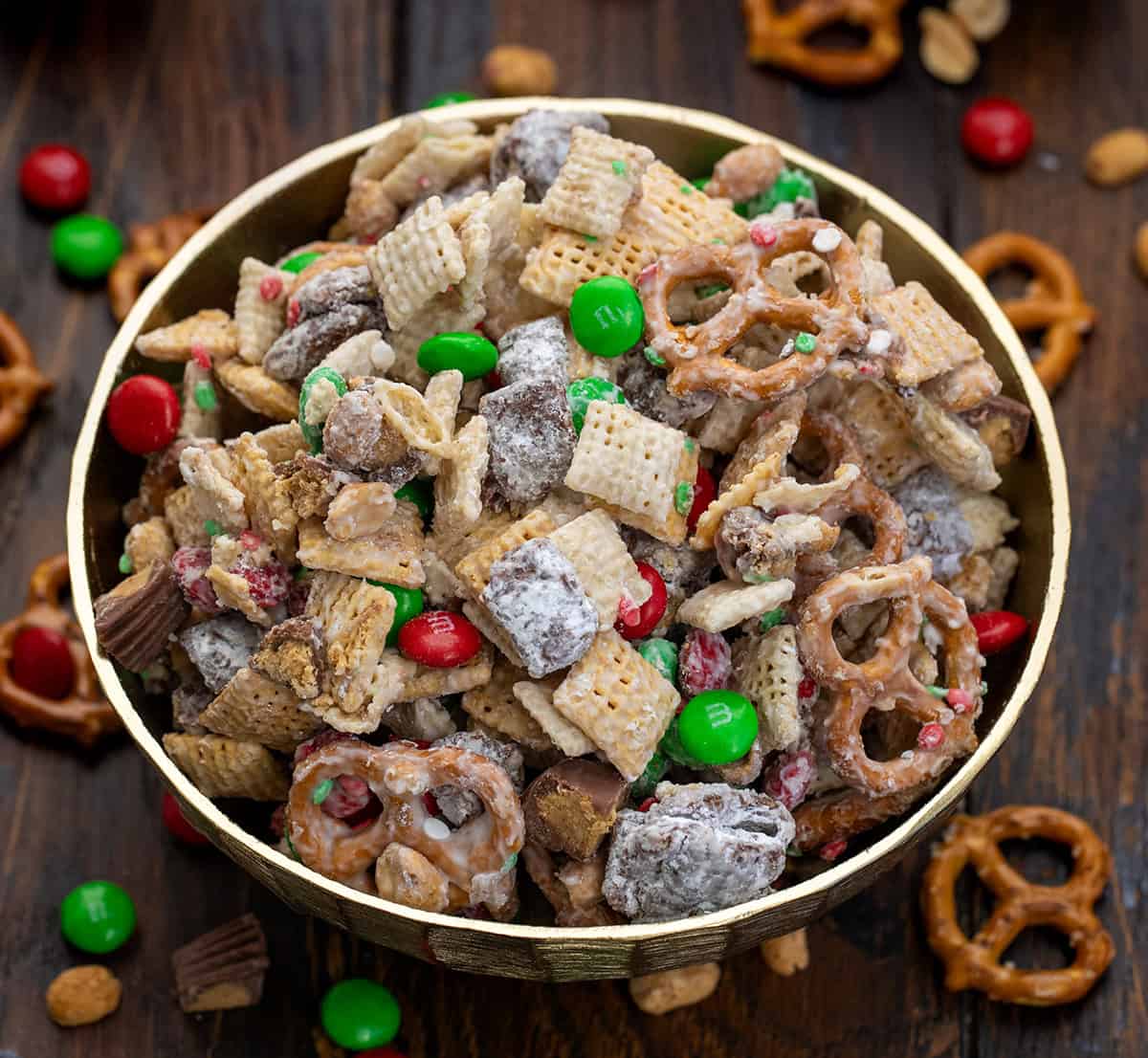 This Ultimate Christmas Snack Mix is what happens when all of my favorite holiday treats collide into one bowl. It’s sweet, salty, crunchy, and truly over-the-top... combining classic peanut butter puppy chow, glossy white chocolate-coated Chex, salty pretzels, peanuts, and festive holiday candies! Gold Bowl filled with Ultimate Christmas Snack Mix on a wooden table with Christmas decorations.