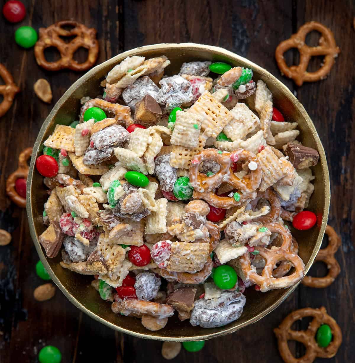 Gold Bowl filled with Ultimate Christmas Snack Mix on a wooden table with Christmas decorations.