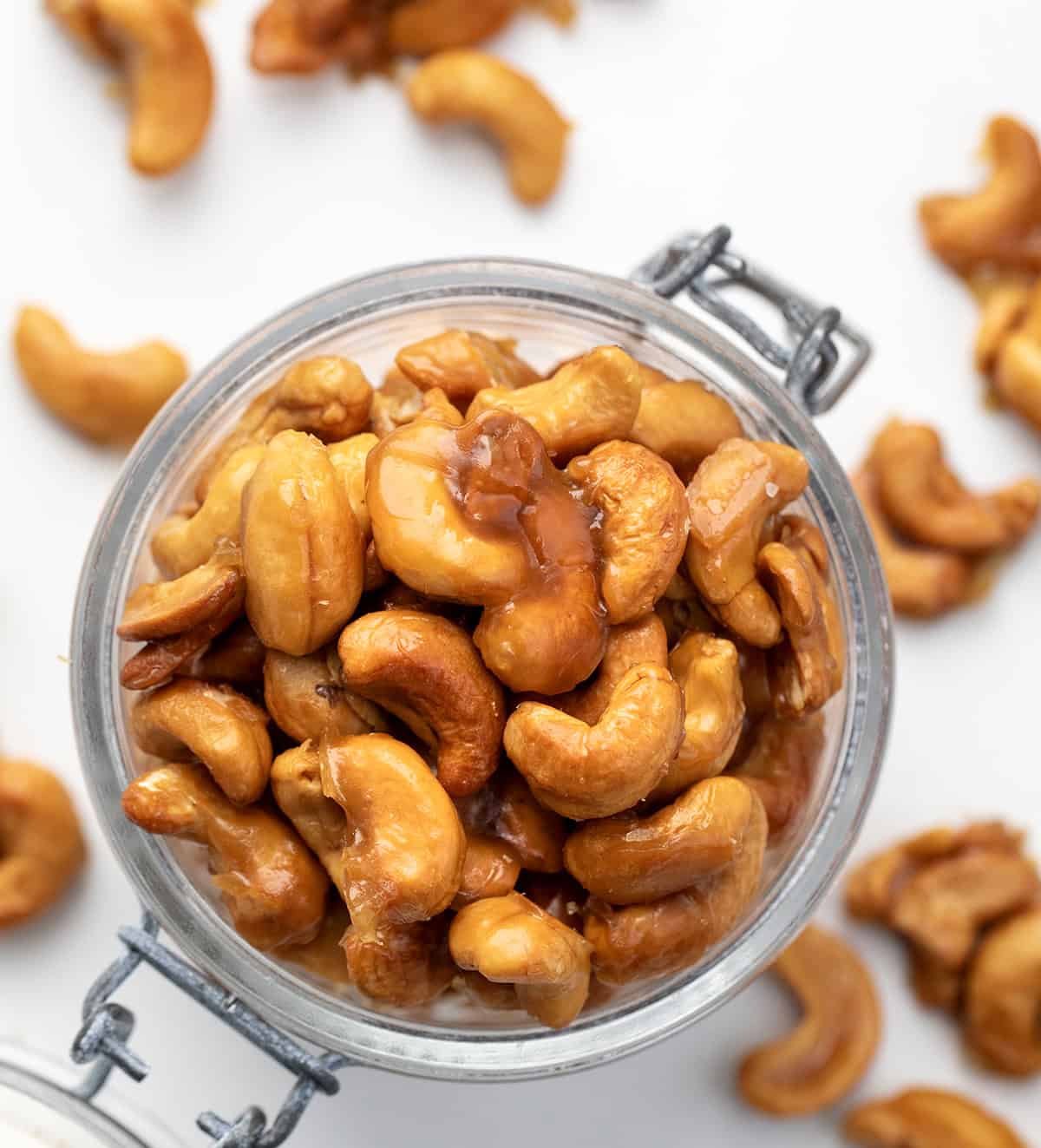Candied Cashews are sweet, crunchy, and totally addictive. A quick toss in honey, brown sugar, and butter turns raw cashews into a golden, caramel-y snack that’s perfectly delicious! Looking down on a full jar of Candied Cashews on a white table.