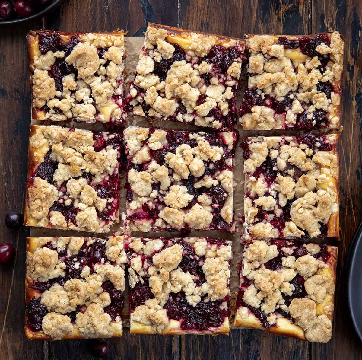 Cranberry Cheesecake Bars cut into squares on a wooden table from overhead.