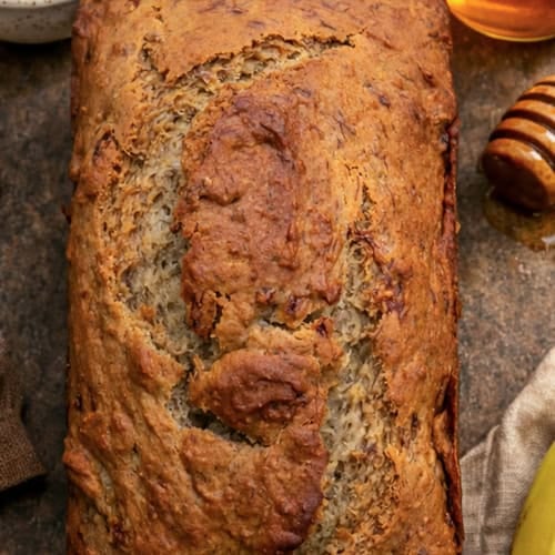 Loaf of Honey Banana Bread with honey and butter next to it.