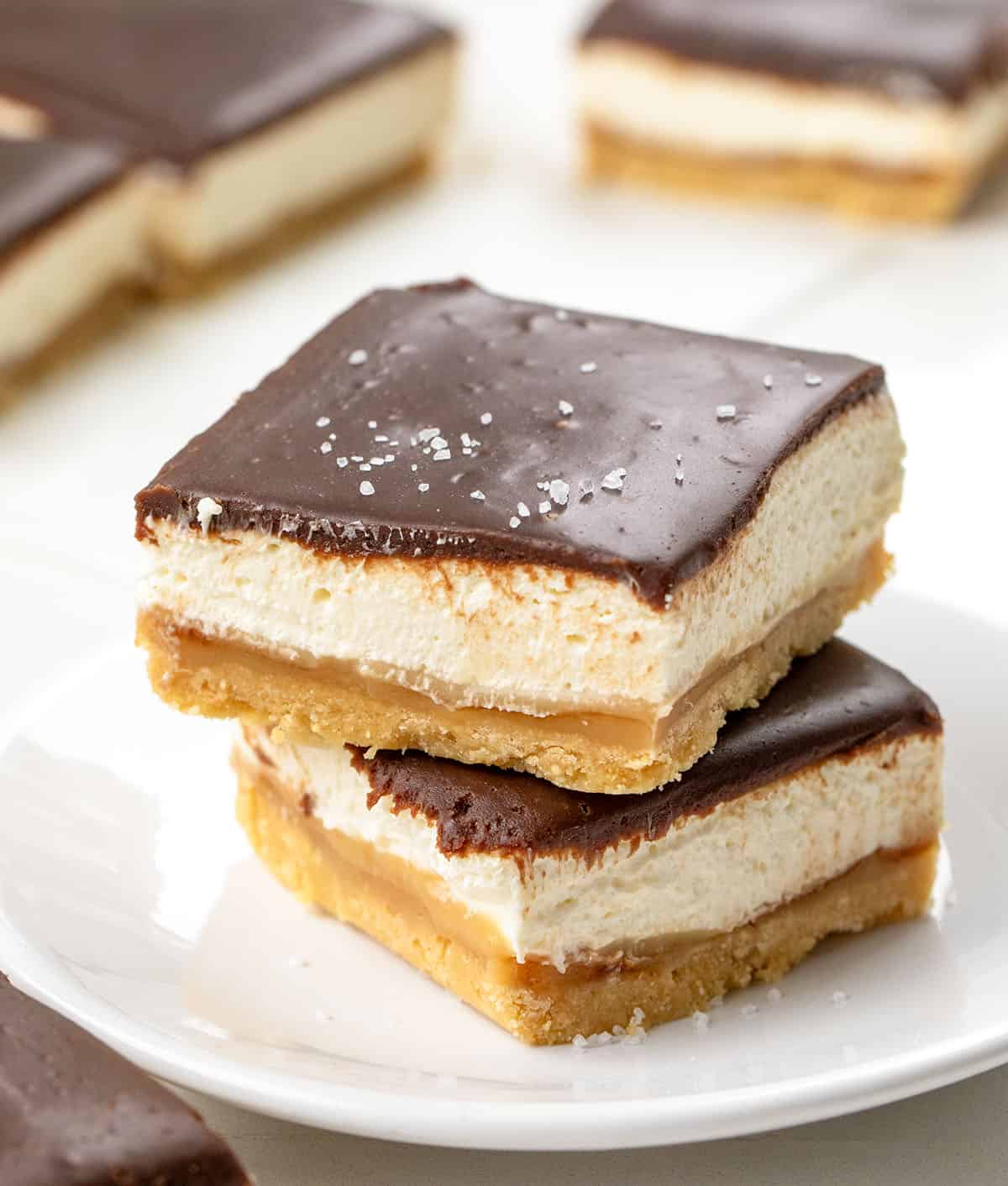 Millionaire's Cheesecake Bars stacked on a small white plate on a white table.
