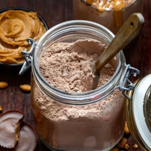 Jar of Peanut Butter Hot Cocoa Mix with a wooden spoon in it with peanut butter in the background.