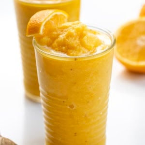 Glasses of Pineapple Ginger Turmeric Smoothie with orange garnish.