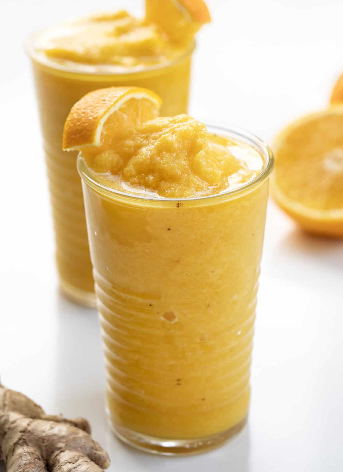 Glasses of Pineapple Ginger Turmeric Smoothie with orange garnish.