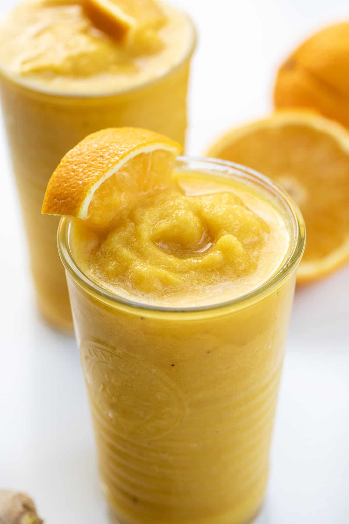 Close up of a glass of Pineapple Ginger Turmeric Smoothie with an orange wedge.