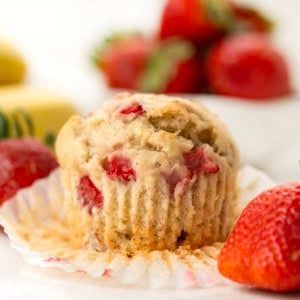 Strawberry Banana Muffin with its wrapper partially pulled off with fresh strawberries and banana.
