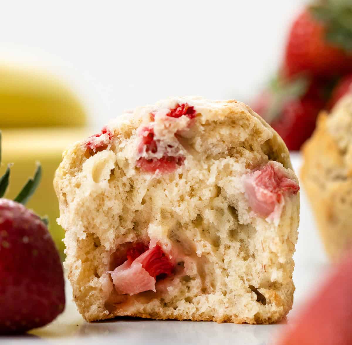 Close up of a Strawberry Banana Muffin torn in half showing tender inside texture and strawberry pieces.