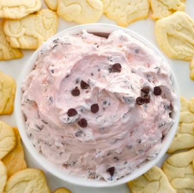 White bowl of Valentine's Booty Dip on a white table surrounded by animal crackers.