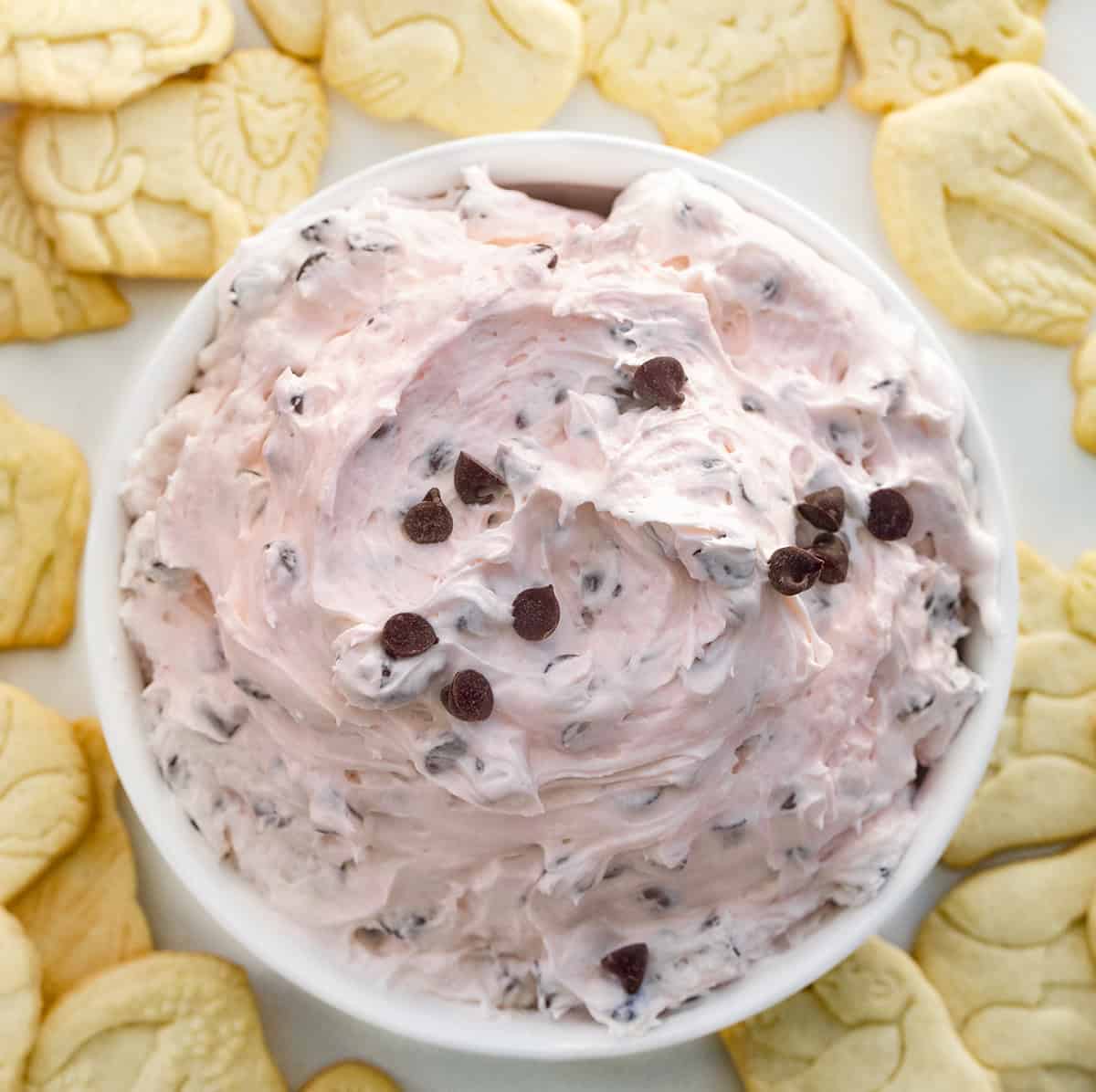 White bowl of Valentine's Booty Dip on a white table surrounded by animal crackers.