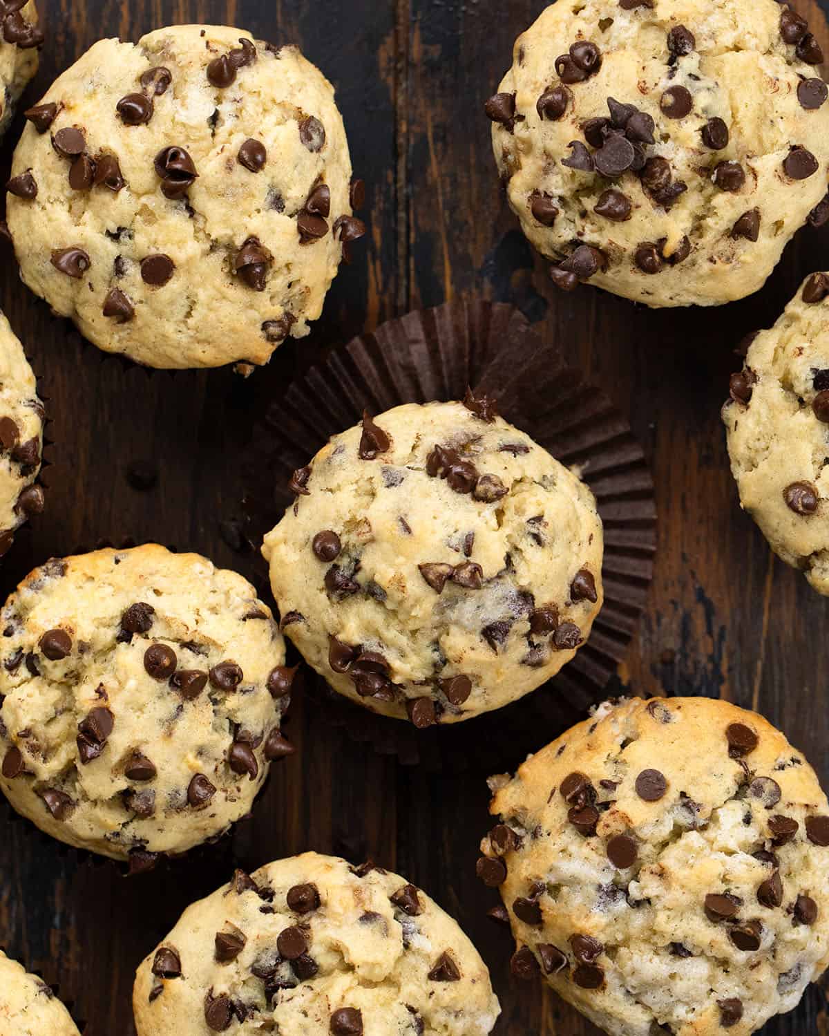 Unwrapped Banana Chocolate Chip Muffin on a wooden table surrounded by more muffins from overhead.