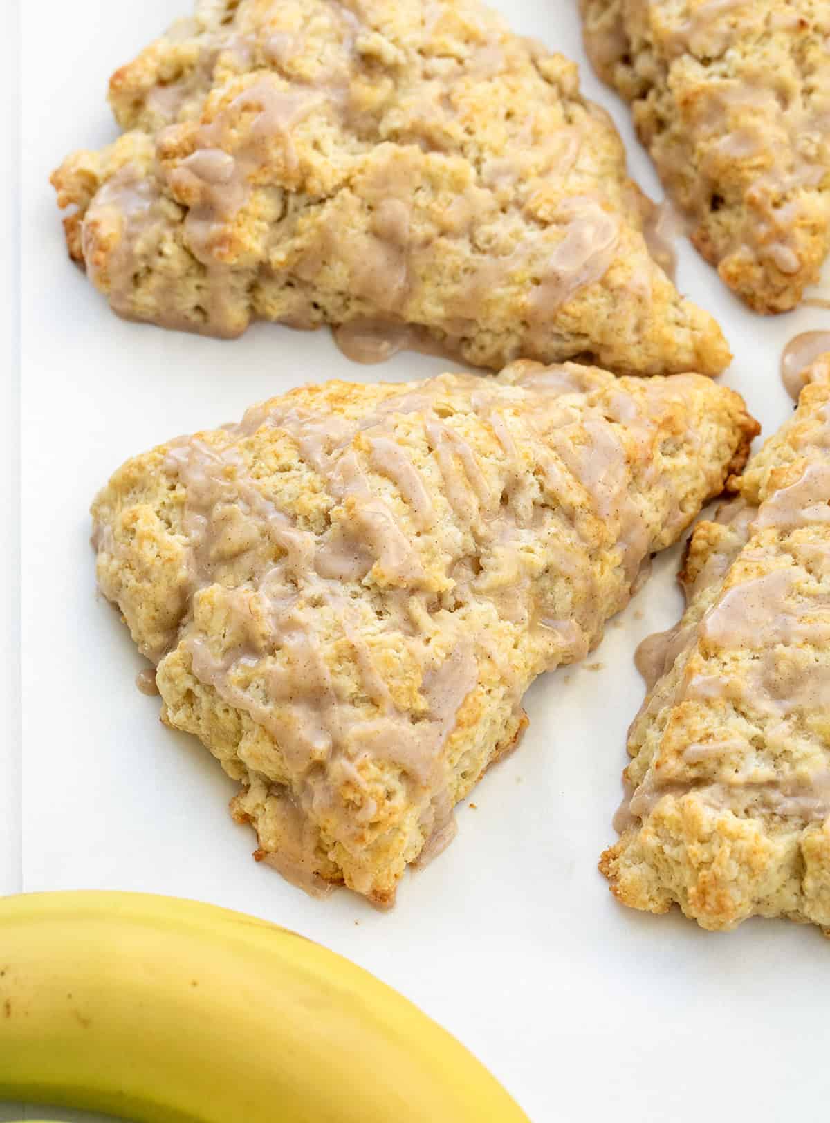 I love these banana scones with maple glaze because they feel like something from a cute bakery case! The edges bake up crisp and golden, and the centers stay soft and tender. The cinnamon maple glaze on top adds sweetness and makes them feel extra special! Banana Scones next to bananas.