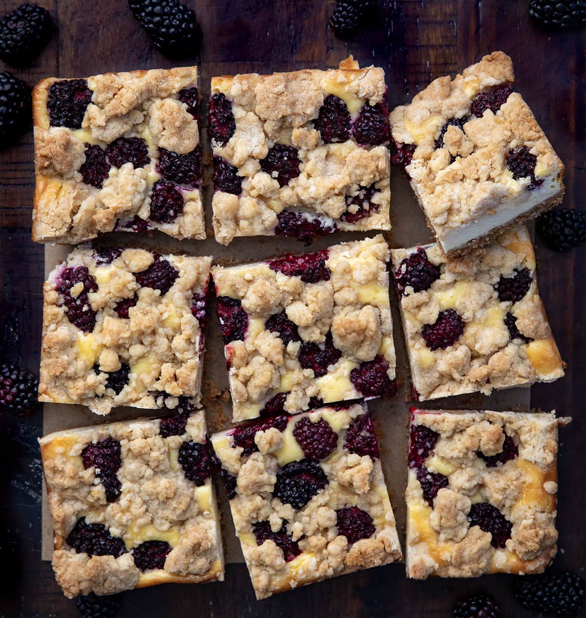 Blackberry Cheesecake Bars are creamy, fruity, and so easy to slice and share. Fresh blackberries add bright pops of flavor to the smooth cheesecake filling and a buttery graham crust that makes every bite irresistible! Blackberry Cheesecake Bars cut into squares on a wooden table from overhead.