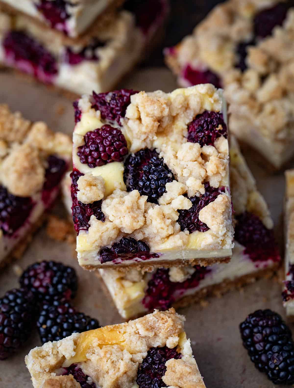 Blackberry Cheesecake Bars are creamy, fruity, and so easy to slice and share. Fresh blackberries add bright pops of flavor to the smooth cheesecake filling and a buttery graham crust that makes every bite irresistible! Looking down on a stack of Blackberry Cheesecake Bars.
