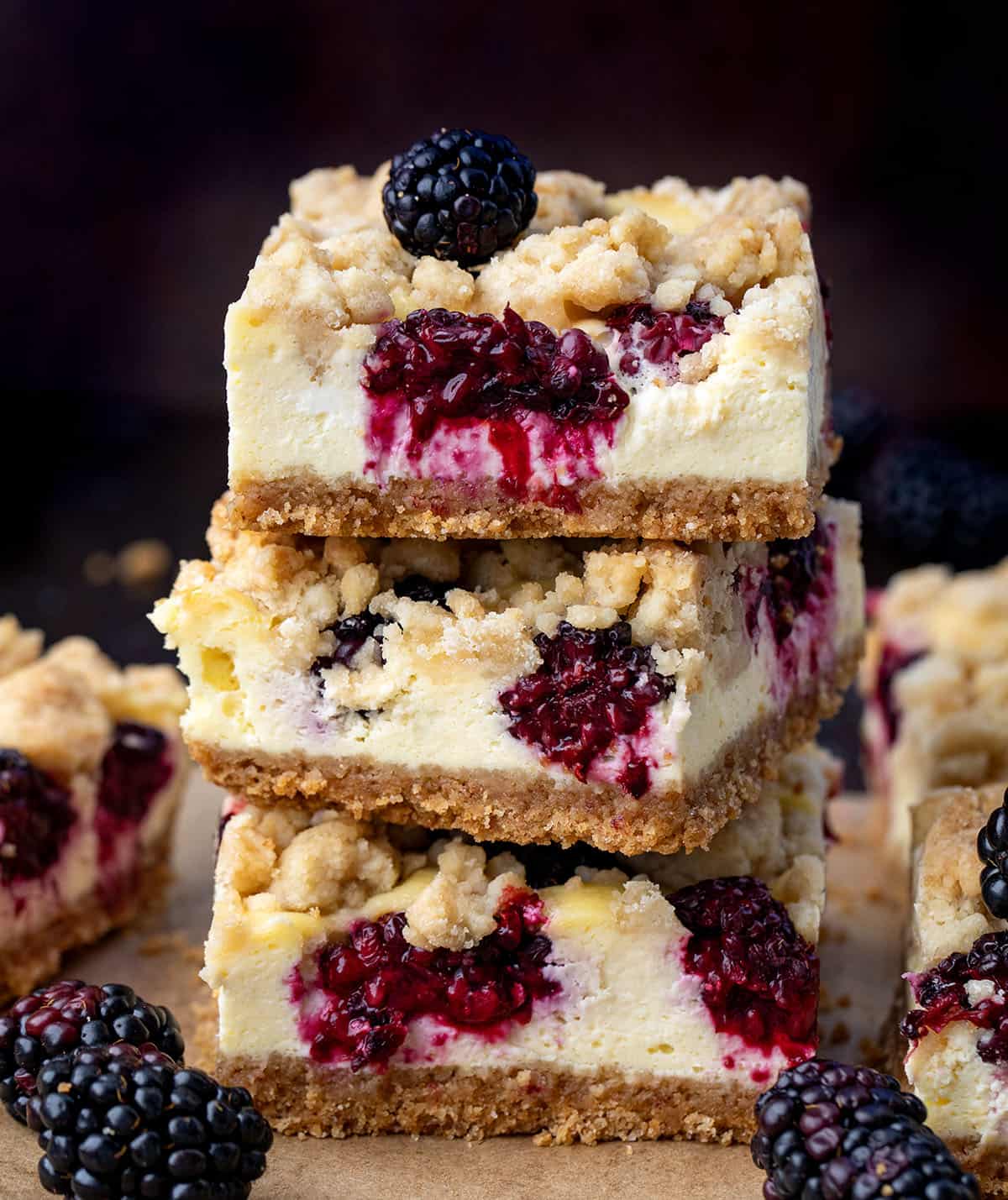 Blackberry Cheesecake Bars are creamy, fruity, and so easy to slice and share. Fresh blackberries add bright pops of flavor to the smooth cheesecake filling and a buttery graham crust that makes every bite irresistible! Stack of Blackberry Cheesecake Bars surrounded by blackberries and more bars.