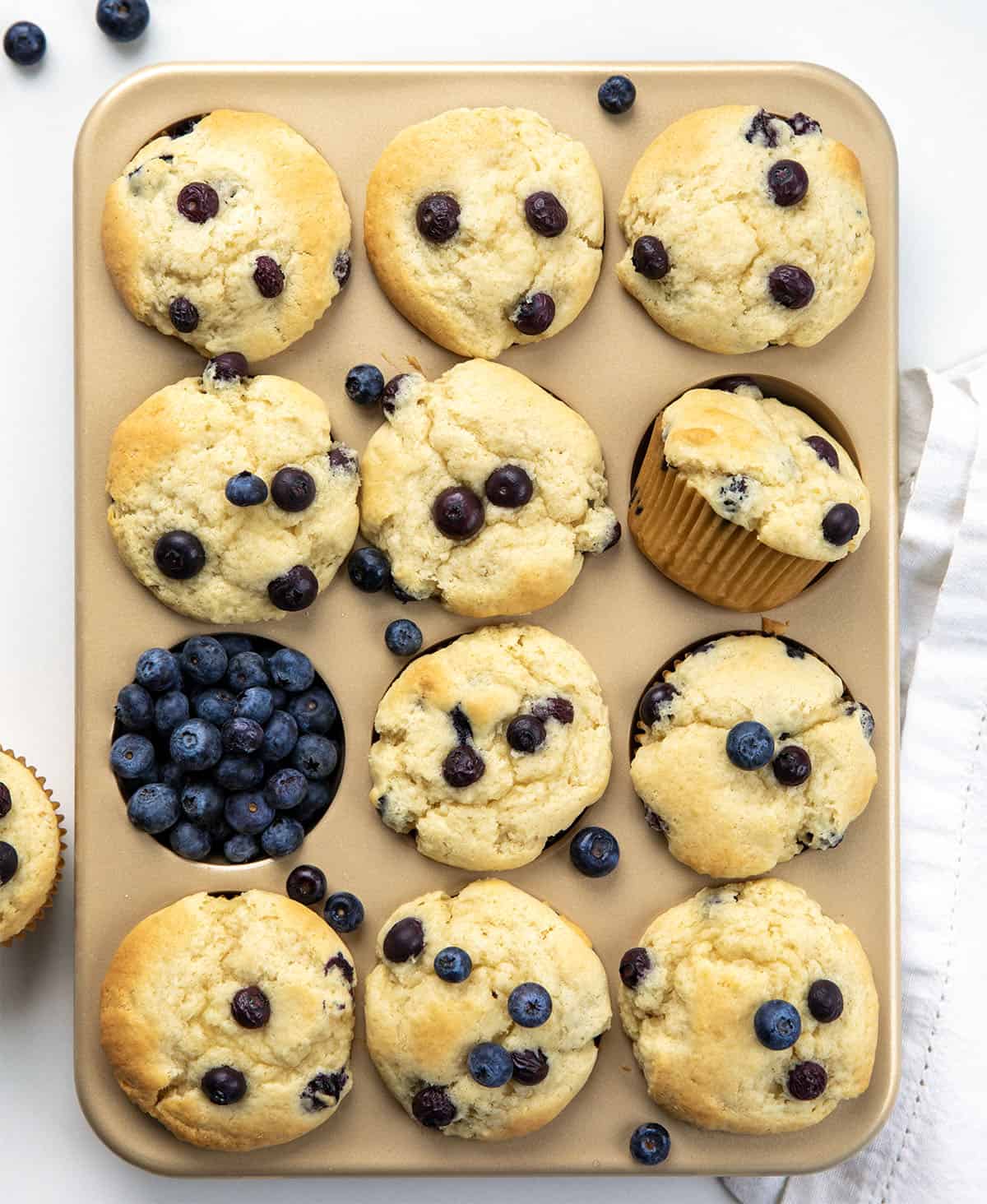 Blueberry Buttermilk Muffins in a muffin tin on a white table from overhead. 