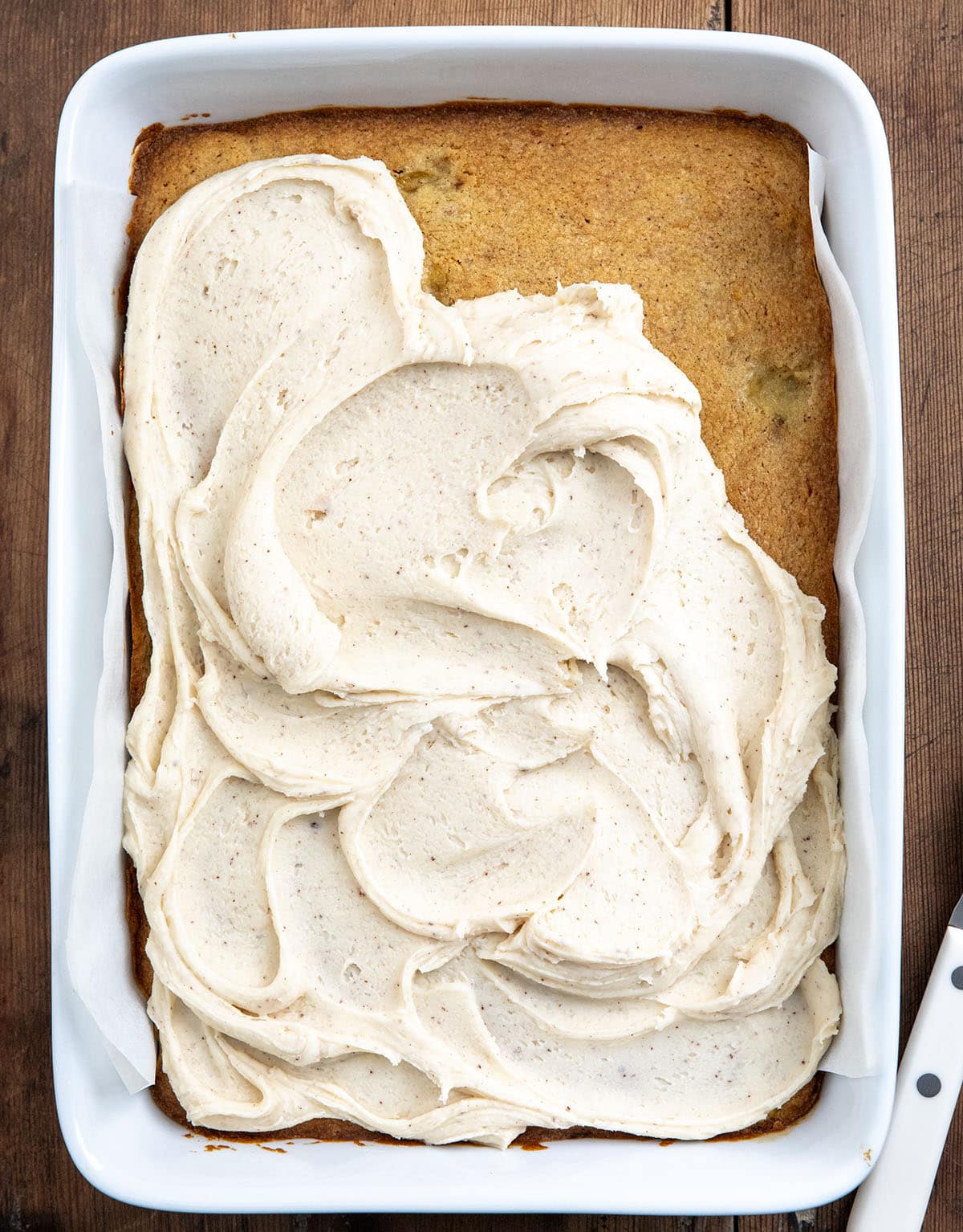 White pan of Browned Butter Banana Bars with Browned Butter Frosting and the frosting is partially covering the bars.