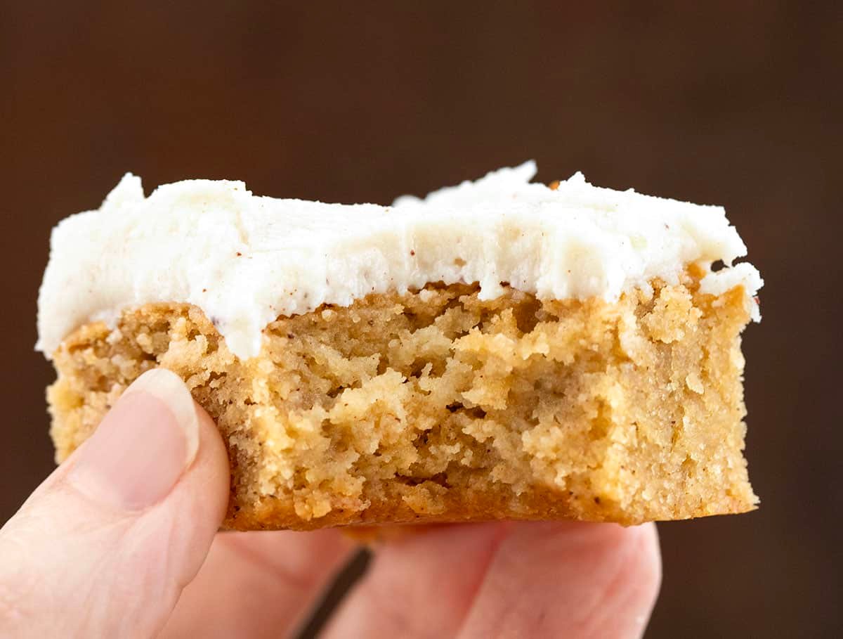 Hand holding a bit into Browned Butter Banana Bars with Browned Butter Frosting.