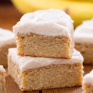 Stack of Browned Butter Banana Bars with Browned Butter Frosting on a wooden table with bananas in the background.