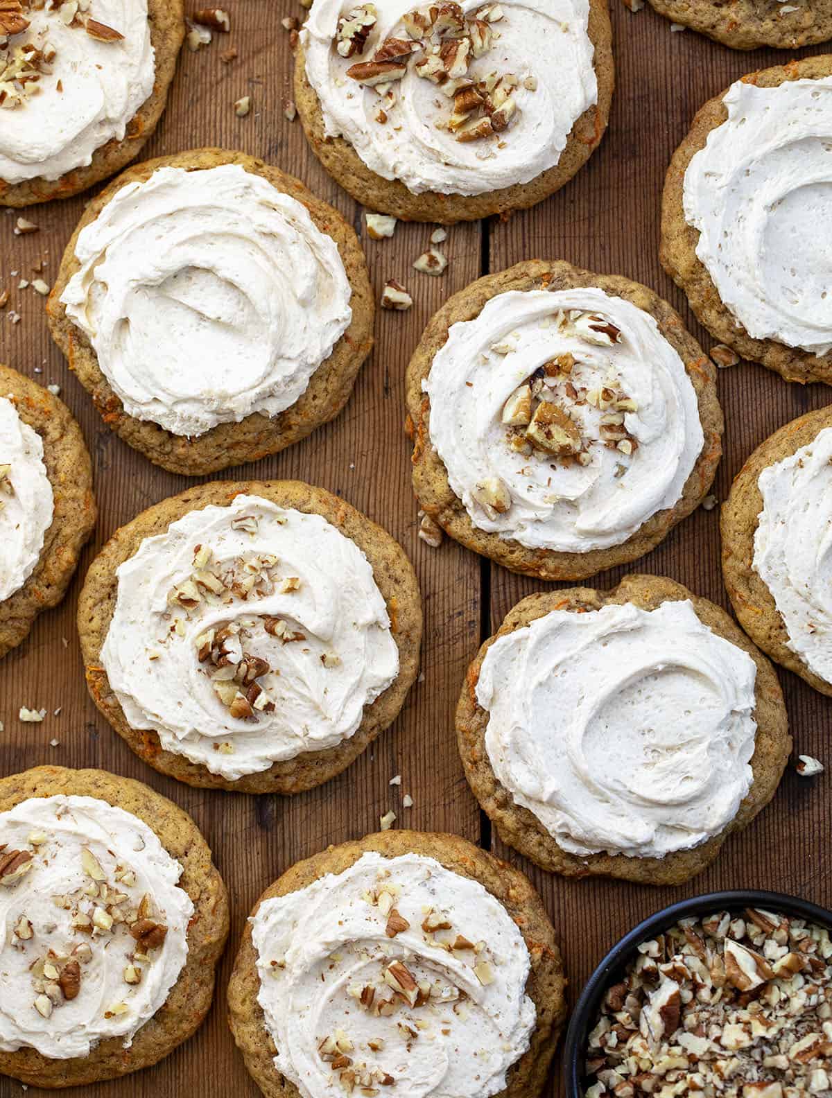Carrot Cake Cookies with Brown Sugar Ermine on a wooden table, some cookies sprinkled with nuts, some plain.