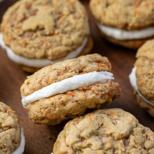 Close up of a Carrot Cake Sandwich Cookie on a wooden table surrounded by more sandwich cookies.