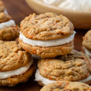 Group of Carrot Cake Sandwich Cookies with a bowl of frosting in the background.