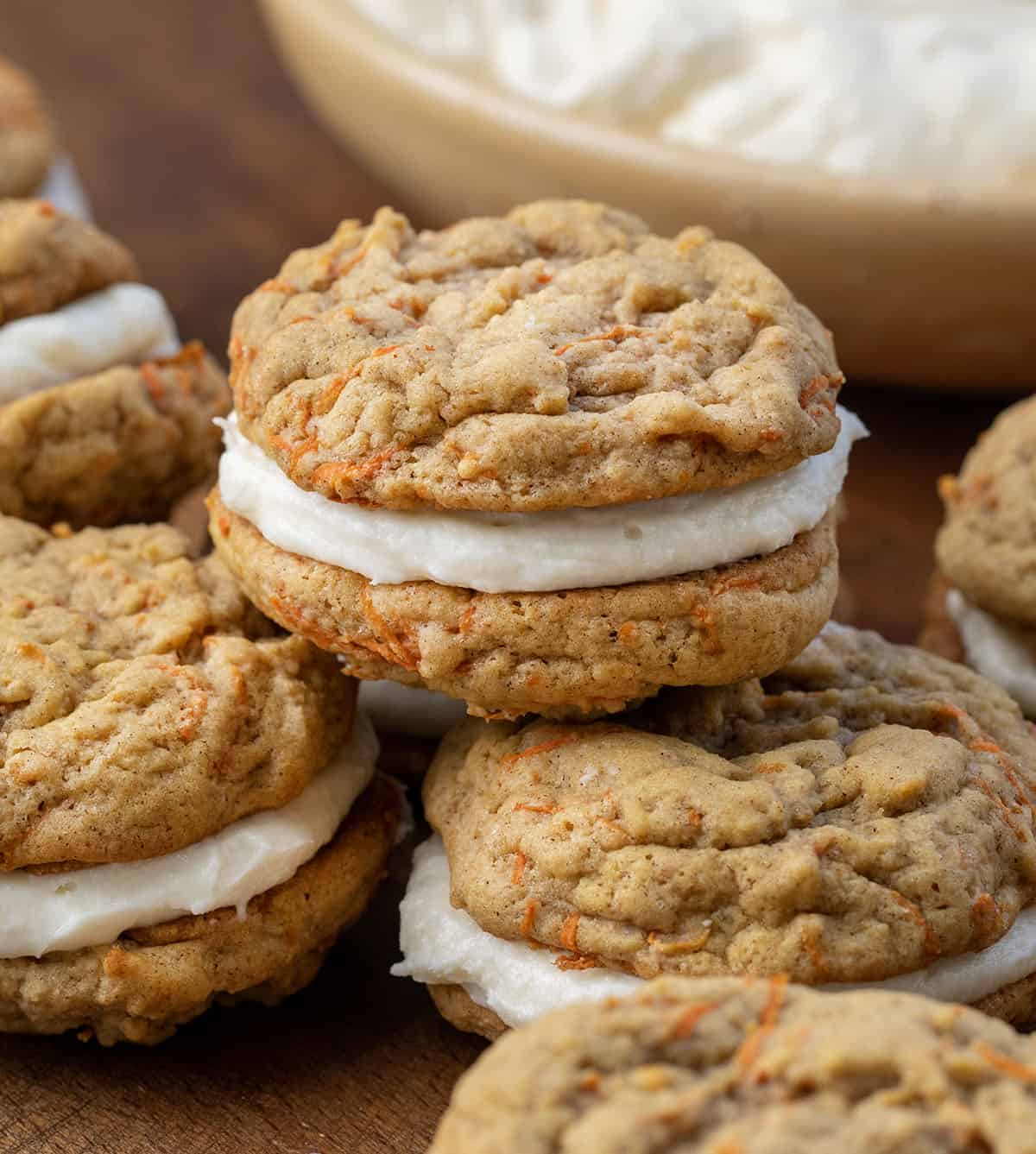 Group of Carrot Cake Sandwich Cookies with a bowl of frosting in the background.