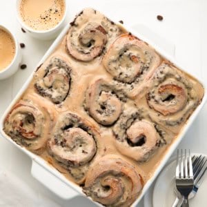 White pan of Chocolate Espresso Rolls on a white table with coffee cups and beans.