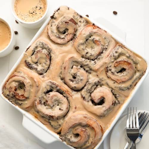 White pan of Chocolate Espresso Rolls on a white table with coffee cups and beans.