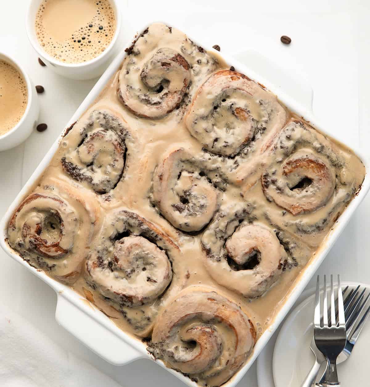 White pan of Chocolate Espresso Rolls on a white table with coffee cups and beans.