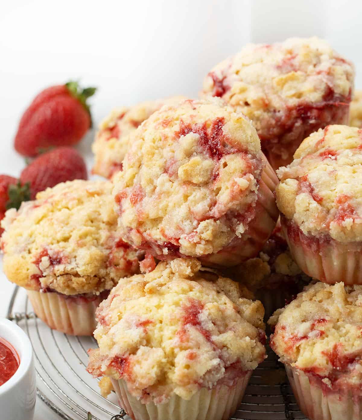 Stack of Double Strawberry Muffins on a cooling rack on a white table.