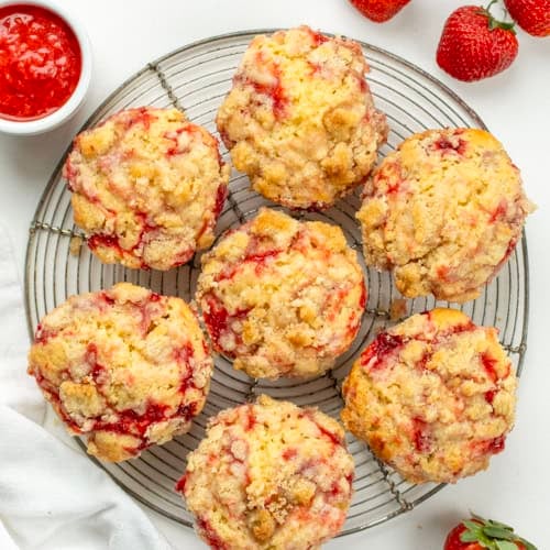 Double Strawberry Muffins on a round wire rack on a white table with strawberry sauce and fresh strawberries.