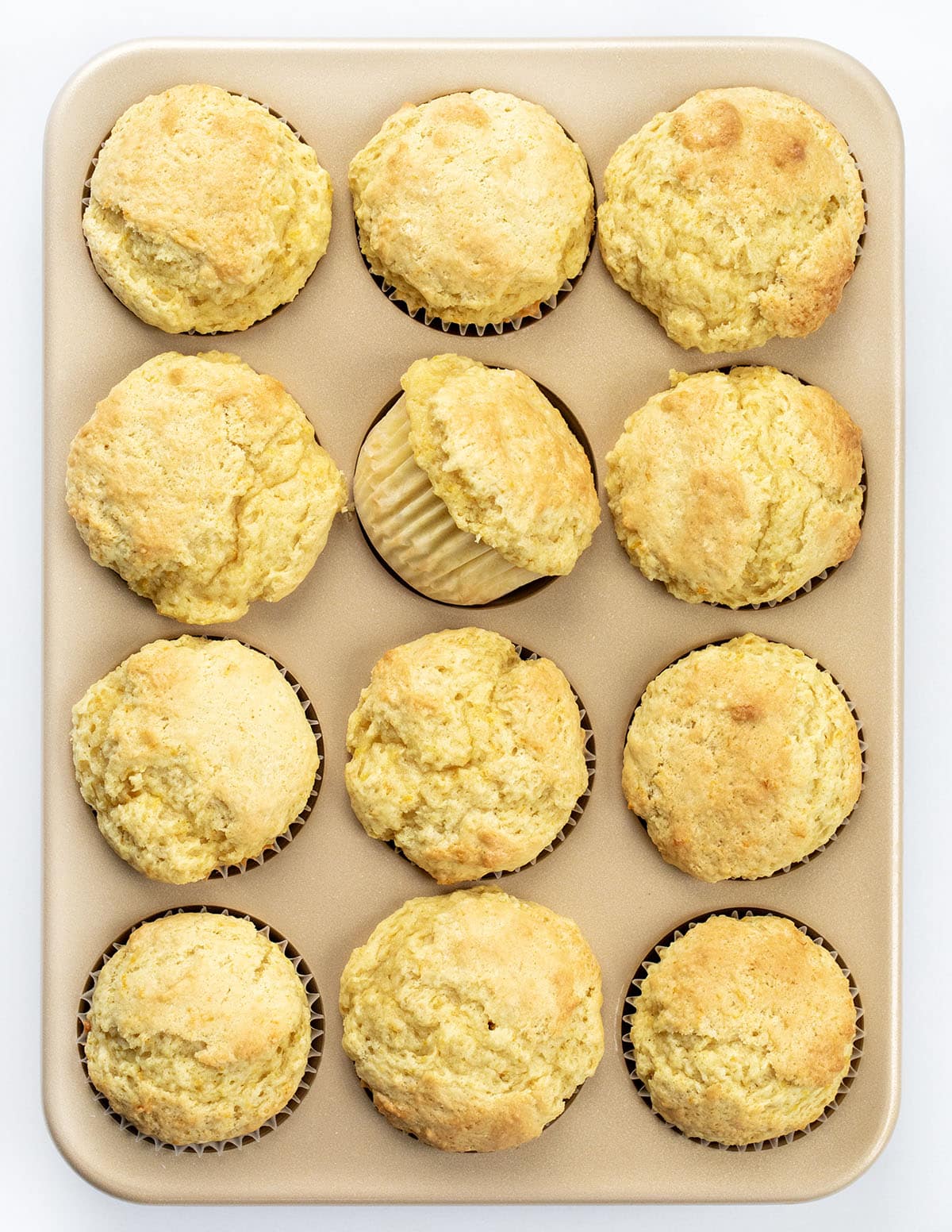 Bright, fluffy, and bursting with fresh orange flavor, these orange vanilla buttermilk muffins are a bakery-style treat you can make right at home. The combination of citrus zest, warm vanilla, and tender buttermilk crumb makes every bite soft, citrusy, and completely irresistible! Pan of Orange Vanilla Buttermilk Muffins on a white table from overhead.