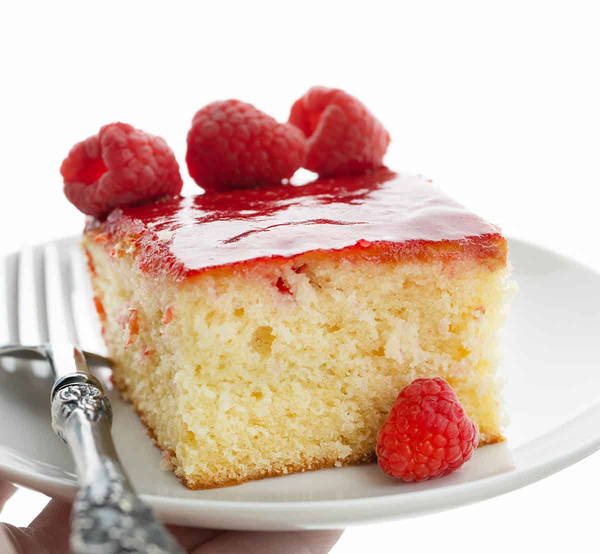 Hand holding a white plate with Raspberry Sauce Cake on it and fresh raspberries.
