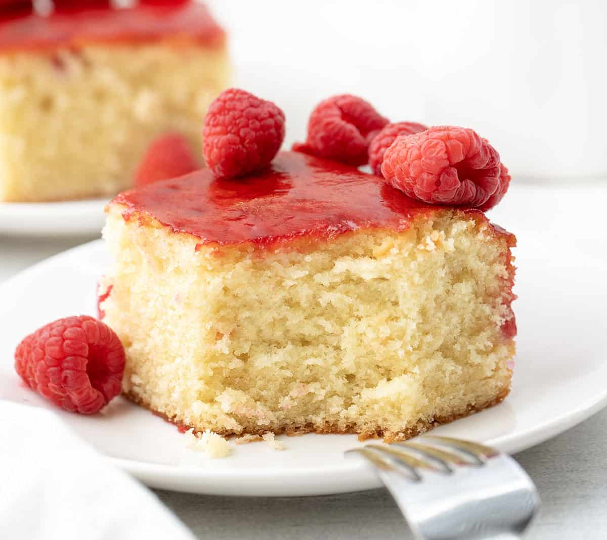 Close up of a piece of Raspberry Sauce Cake with a bite taken out it and fork reting on white plate.