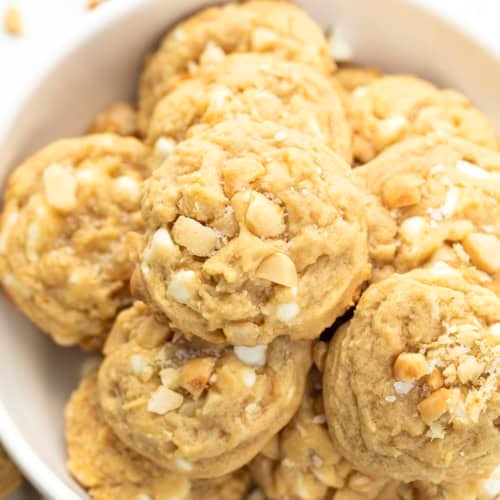 White bowl of Salted Honey White Chocolate Macadamia Nut Cookies on a white table.