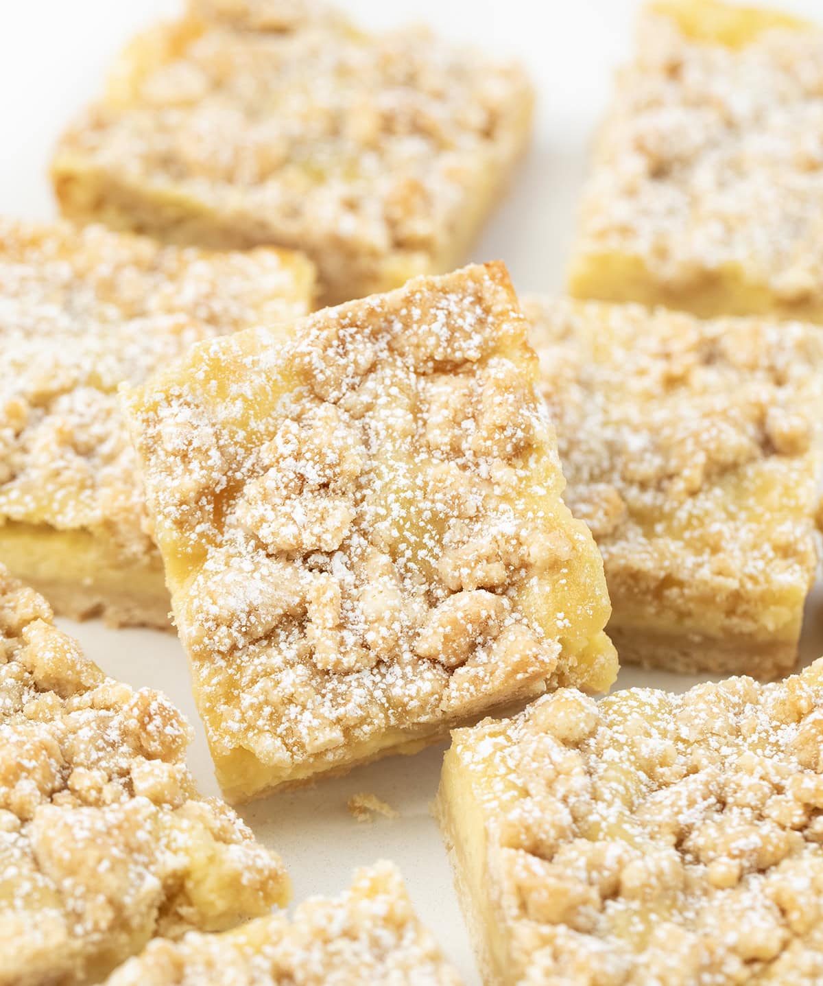 These Vanilla Cream Crumb Bars start with a buttery shortbread crust layered with a smooth vanilla custard filling, and are finished with a golden brown crumble topping! Close up of a Vanilla Cream Crumb Bar leaned up against other bars.