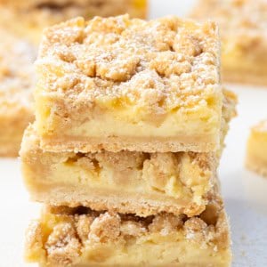 Stack of Vanilla Cream Crumb Bars on a white table surrounded by other bars.