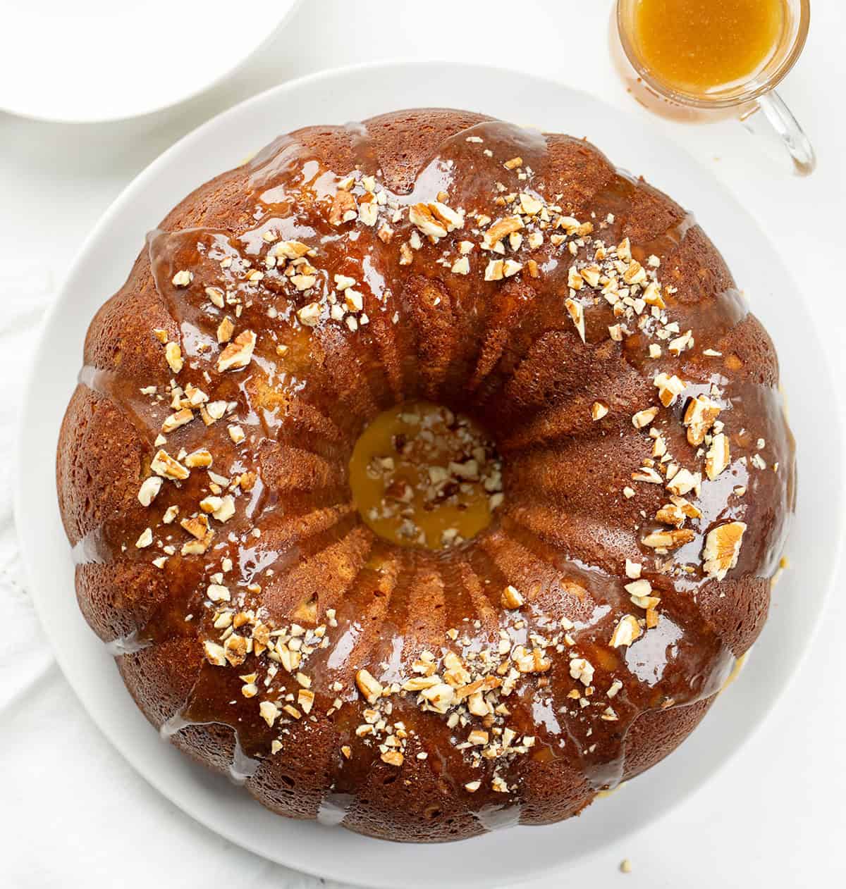 This banana Bundt cake is incredibly moist, packed with ripe banana flavor, and finished with a warm brown sugar glaze that drips into every groove! Banana Bundt Cake covered in Brown Butter Glaze on a white table from overhead.
