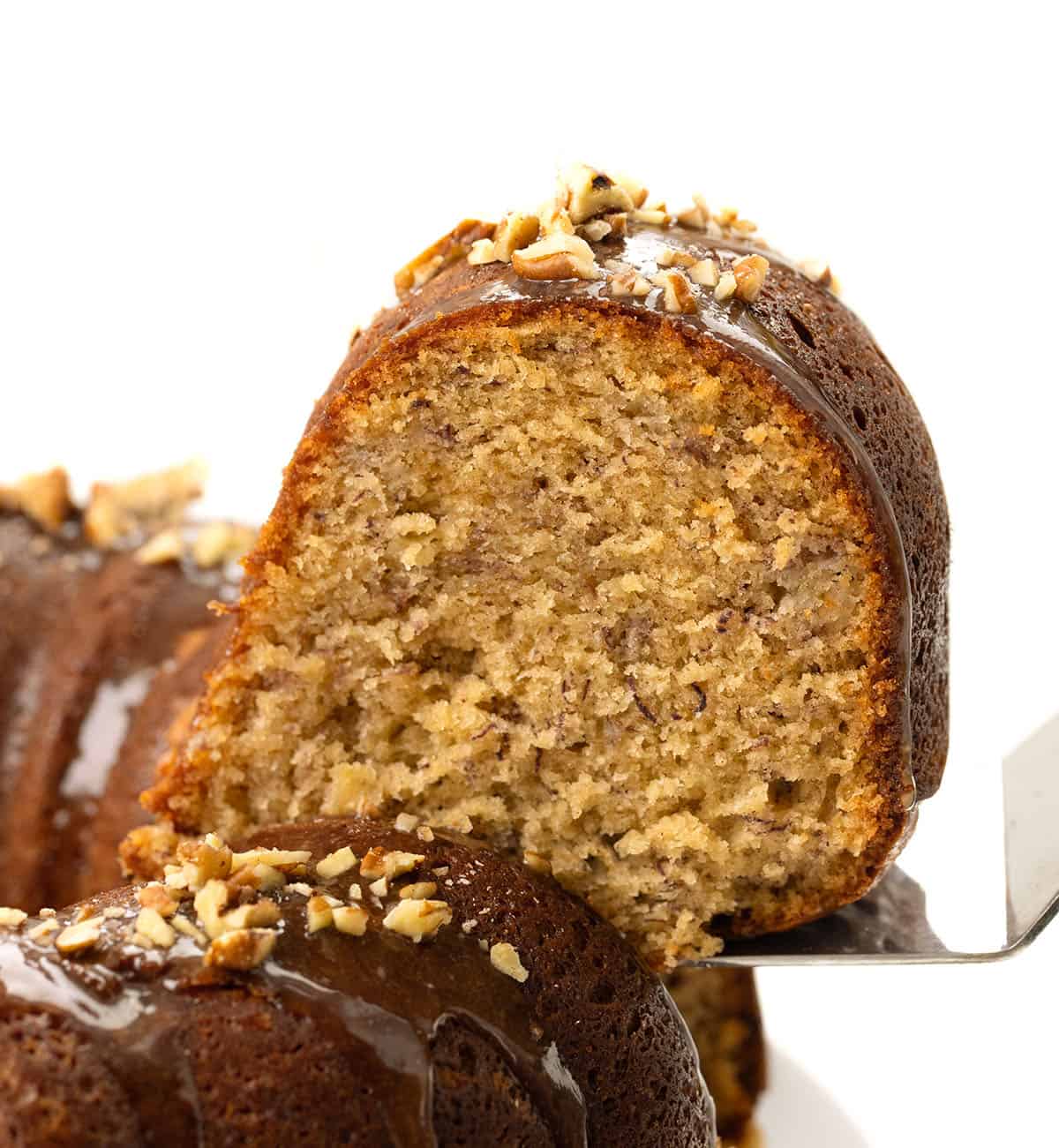 Picking up a piece of Banana Bundt Cake covered in brown sugar glaze and chopped nuts.