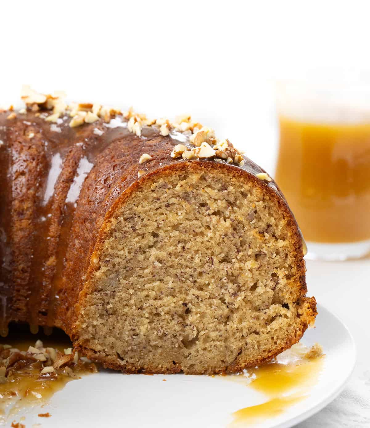 This banana Bundt cake is incredibly moist, packed with ripe banana flavor, and finished with a warm brown sugar glaze that drips into every groove! Cut into Banana Bundt Cake on a white plate showing tender texture inside.
