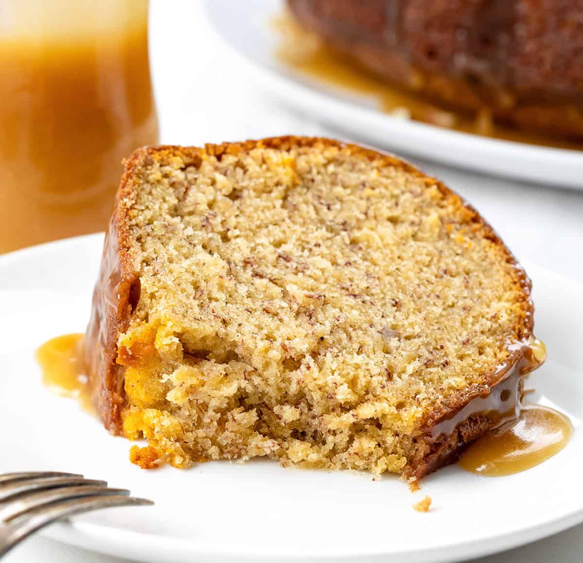 This banana Bundt cake is incredibly moist, packed with ripe banana flavor, and finished with a warm brown sugar glaze that drips into every groove! Piece of Banana Bundt Cake laying on a plate and a bite removed showing just how tender the cake is.