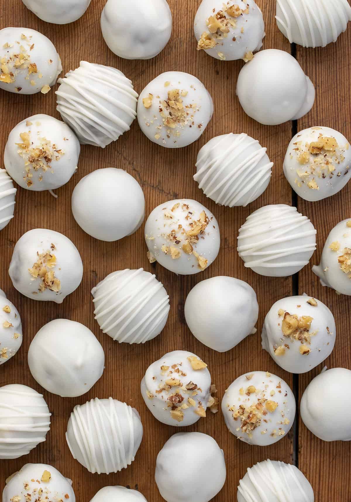 These Carrot Cake Truffles turn classic carrot cake into sweet, bite-sized treats! Made with homemade carrot cake, creamy frosting, and dipped in smooth vanilla bark, theyโre perfect for Easter, spring parties, or whenever youโre craving a little dessert. Carrot Cake Truffles with chopped nuts and chocolate drizzle on a wooden table from overhead.
