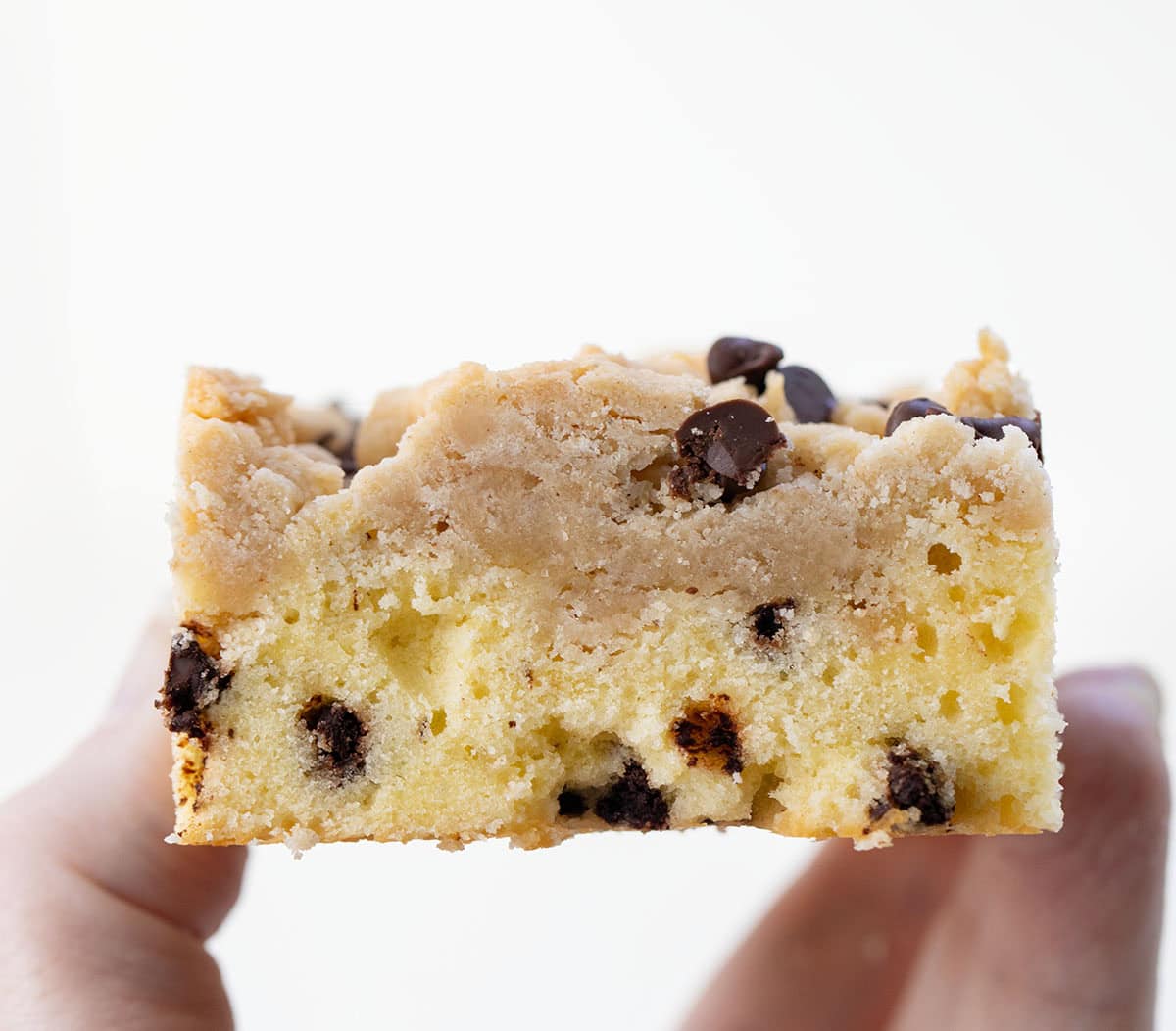 Hand holding a Chocolate Chip Crumb Cake bar very close up showing tender texture.