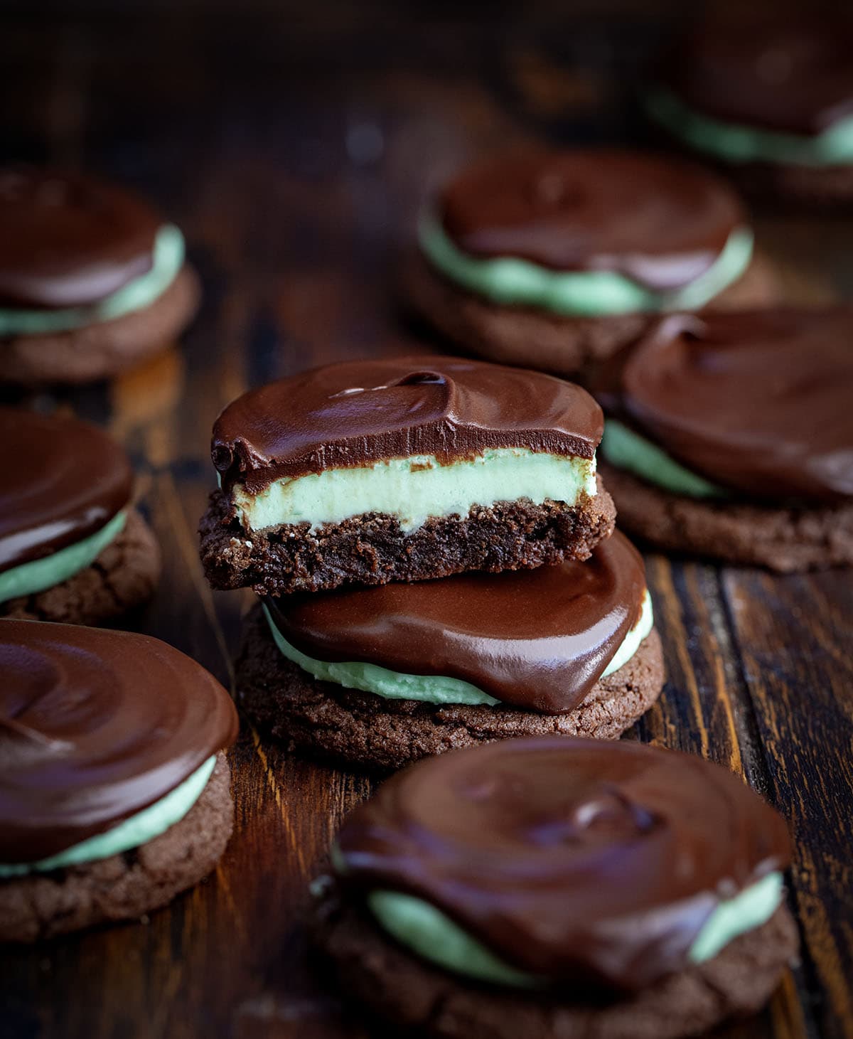 These Chocolate Mint Cookies (Grasshopper Cookies) are a chocolate lover’s dream! Start with soft, cocoa-rich cookies, add a fluffy peppermint filling, and finish with a silky chocolate ganache layer that makes each bite feel extra special! Chocolate Mint Cookies on a wooden table with one cookie cut in half showing the layers.