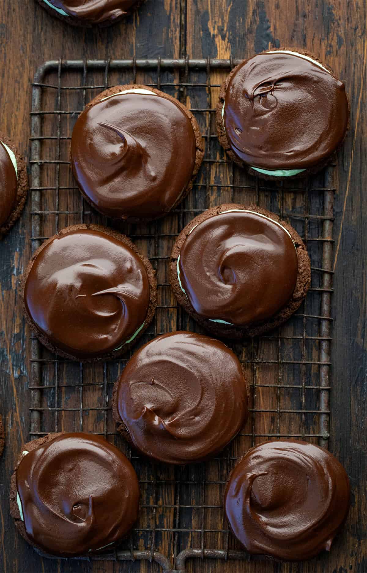 These Chocolate Mint Cookies (Grasshopper Cookies) are a chocolate lover’s dream! Start with soft, cocoa-rich cookies, add a fluffy peppermint filling, and finish with a silky chocolate ganache layer that makes each bite feel extra special! Chocolate Mint Cookies on a cooling rack on a wooden table from overhead.